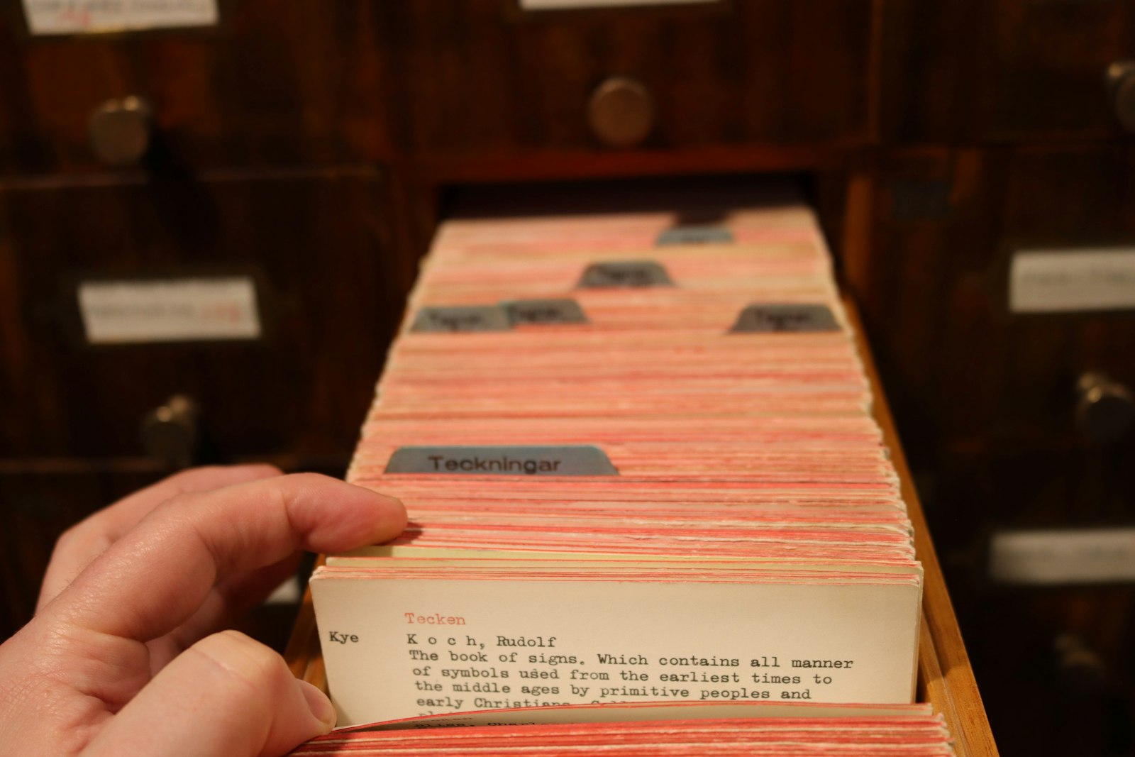 Een hand trekt één kaart uit een houten kaartenbak in een bibliotheek