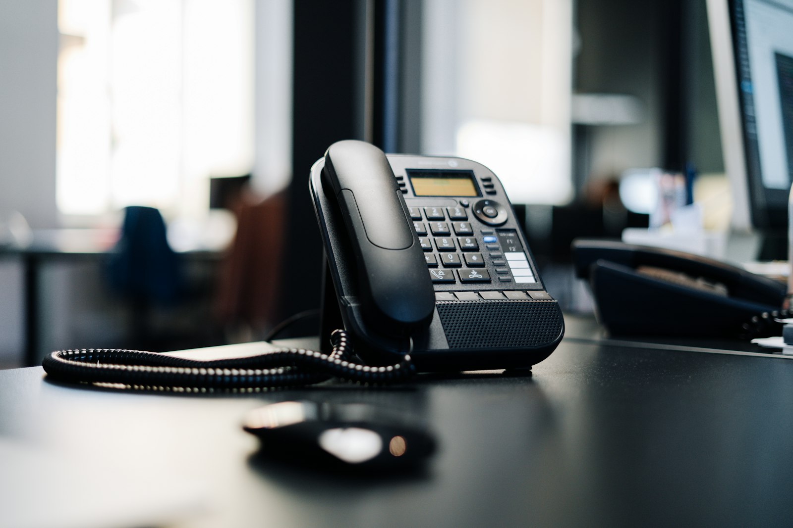Een zwarte bureautelefoon op een donkere houten tafel