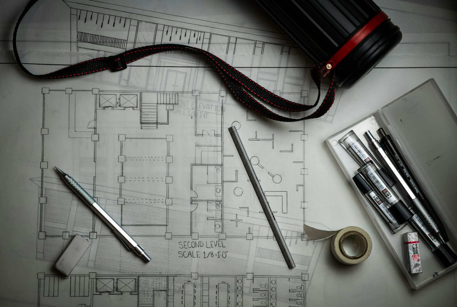 Bouwtekeningen op een werktafel met potloden, een metalen liniaal en een tekeningkoker